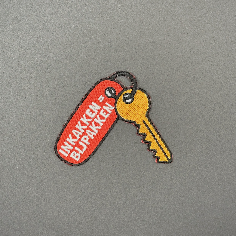 Embleem sleutel met sleutelhanger met text: "inkakken = bijpakken"