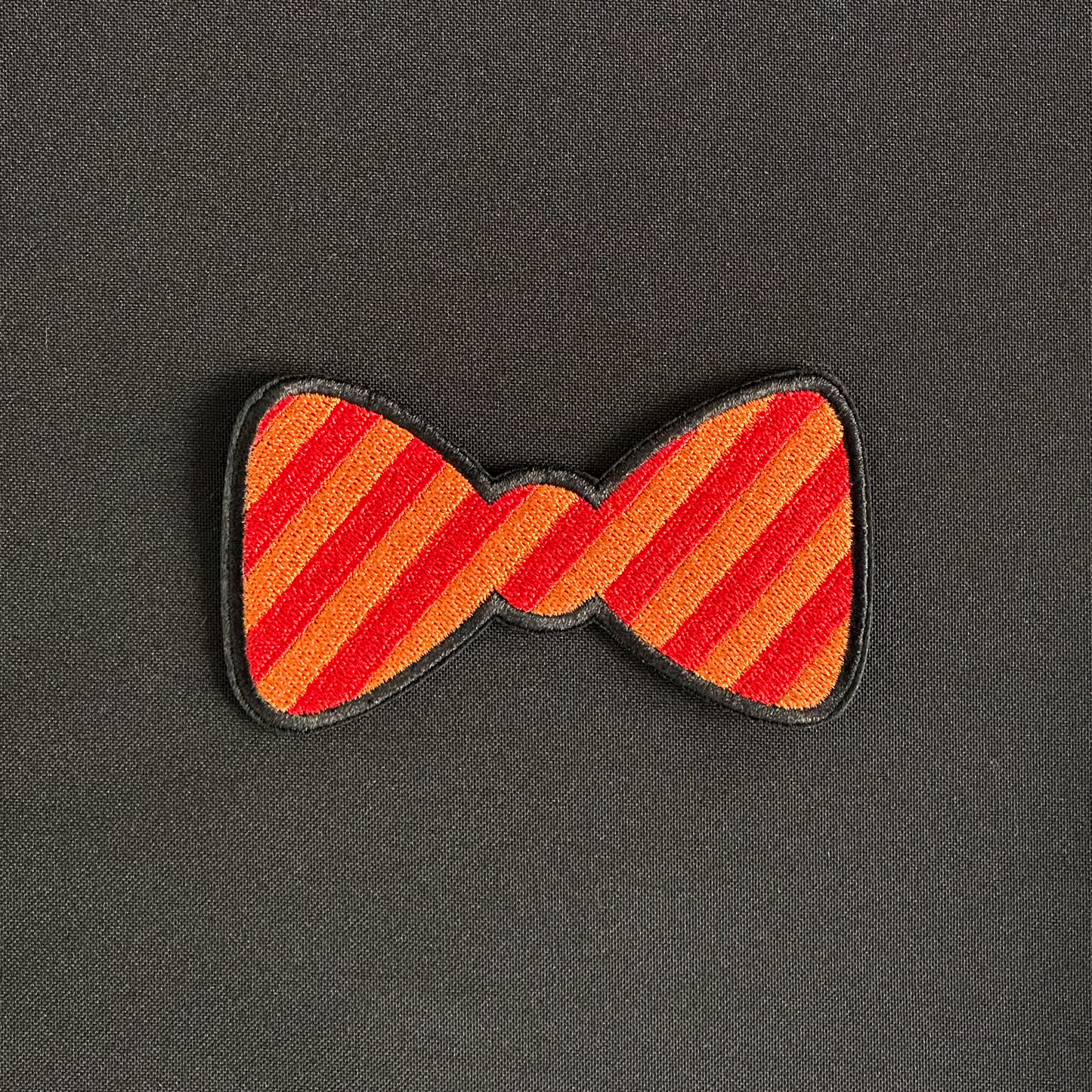 Een Kielegat embleem in de vorm van een strikje die rood en oranje gestreept is.