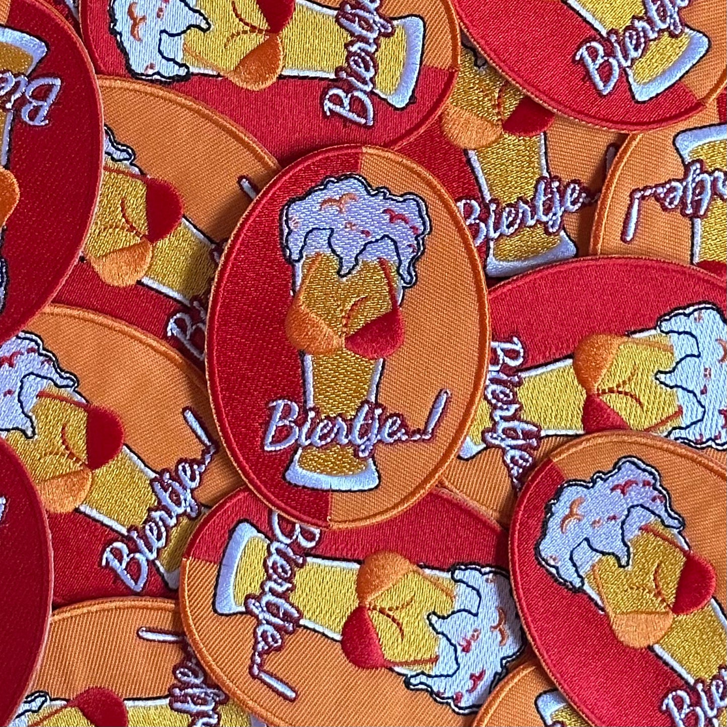 Ovaalvormig Kielegat embleem met rood en oranje achtergrond, waarop een biertje met tieten is afgebeeld, waarbij de tieten een rood - oranje gekleurde BH draagt. Ook is de tekst 'Biertje' op het embleem opgenomen.