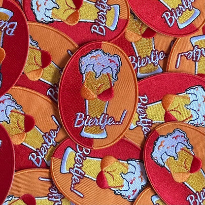 Ovaalvormig Kielegat embleem met rood en oranje achtergrond, waarop een biertje met tieten is afgebeeld, waarbij de tieten een rood - oranje gekleurde BH draagt. Ook is de tekst 'Biertje' op het embleem opgenomen.