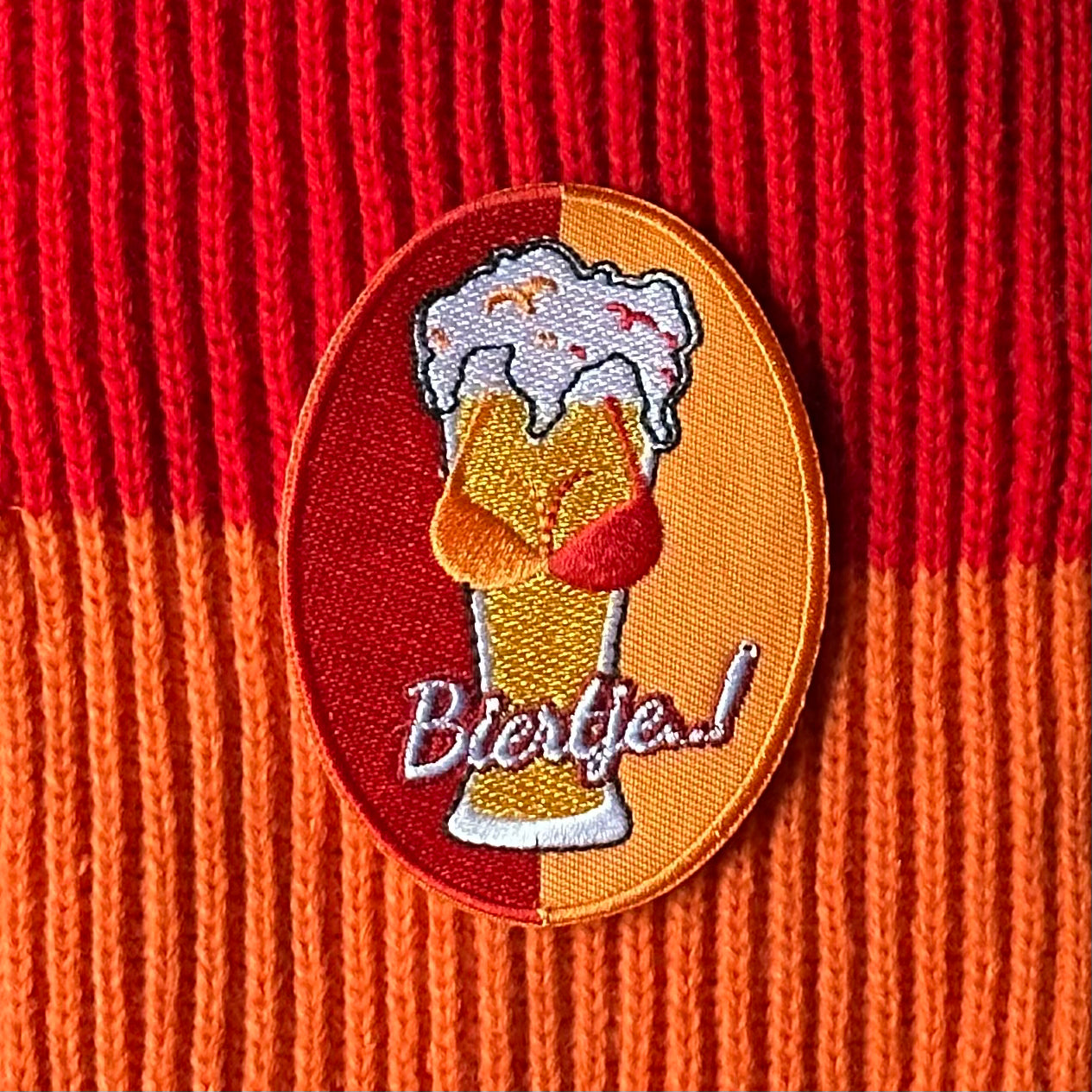 Ovaalvormig Kielegat embleem met rood en oranje achtergrond, waarop een biertje met tieten is afgebeeld, waarbij de tieten een rood - oranje gekleurde BH draagt. Ook is de tekst 'Biertje' op het embleem opgenomen.