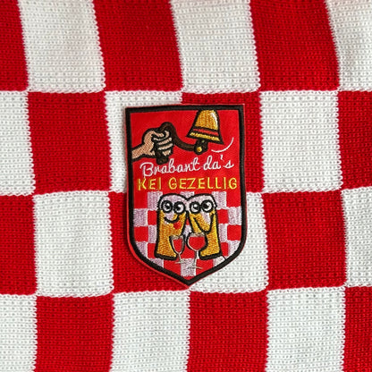 Een rood embleem, waarbij er aan een bel getrokken word, twee biertjes gezellig met een wijntje zitten en de tekst 'Brabant da's KEI GEZELLIG' is opgenomen.