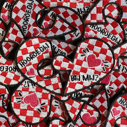 Een in gebroken hart, wat door een puzzel stukje te verbinden is aan elkaar. De achtergrond van dit hartje is een brabantse vlag, en op het linkerhart deel staat de tekst 'Hooroe gij' en op het rechterhart deel staat de tekst 'bij mij?'