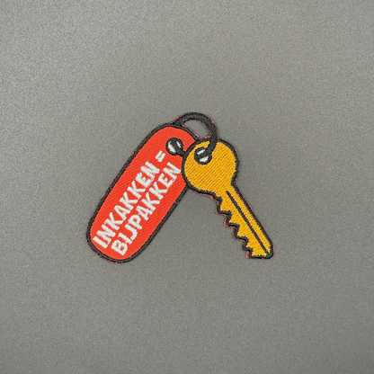 Embleem sleutel met sleutelhanger met text: "inkakken = bijpakken"