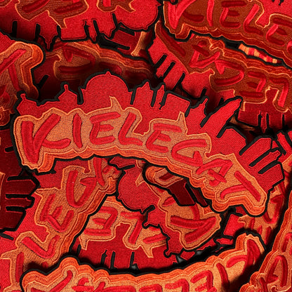 Het Kielegat (rug)embleem. Dit embleem heeft de tekst Kielegat in het rood, met een oranje achtergrond. Daarboven is ook in het rood de kenmerkende Bredase gebouwen opgenomen.