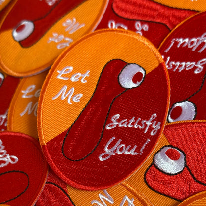 Ovaalvormig Kielegat embleem, met rood en oranje achtergrond, waarop een satisfyer is afgebeeld en de tekst: Let Me Satisfy You!