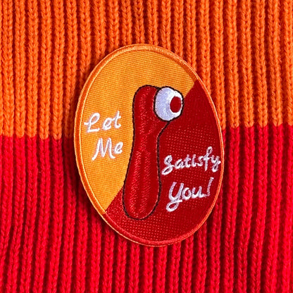 Ovaalvormig Kielegat embleem, met rood en oranje achtergrond, waarop een satisfyer is afgebeeld en de tekst: Let Me Satisfy You!