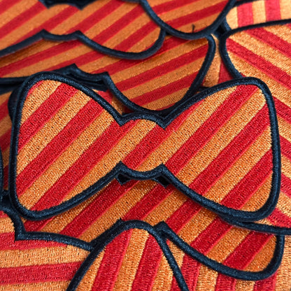 Een Kielegat embleem in de vorm van een strikje die rood en oranje gestreept is.