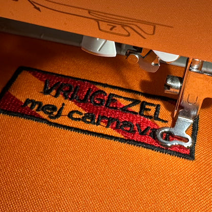 Een rechthoekig spreukenbord, met een rood-oranje gestreepte achtergrond in de Kielegat kleuren. Hierop staat de tekst 'Vrijgezel mej carnval'.