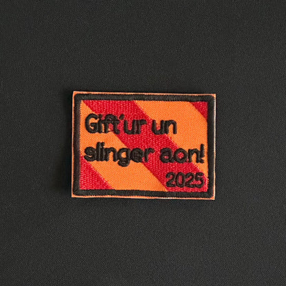 Een rechthoekig spreukenbord, met een rood-oranje gestreepte achtergrond in de Kielegat kleuren. Hierop staat de tekst 'Gift'ur un slinger aon! 2025'.